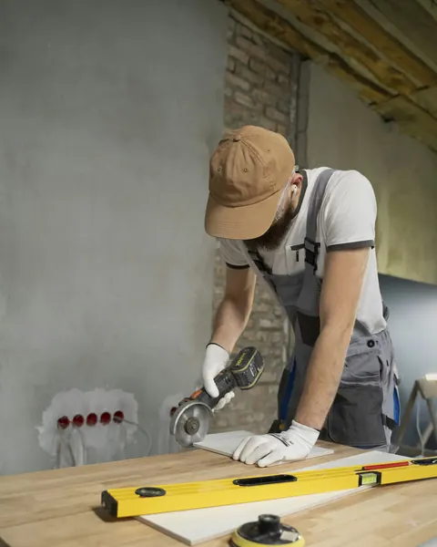 Un carreleur découpe un carreau à la meuleuse sur l’établi du chantier